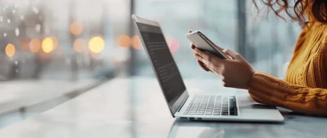 Woman using laptop and smartphone at a desk with blurred city lights